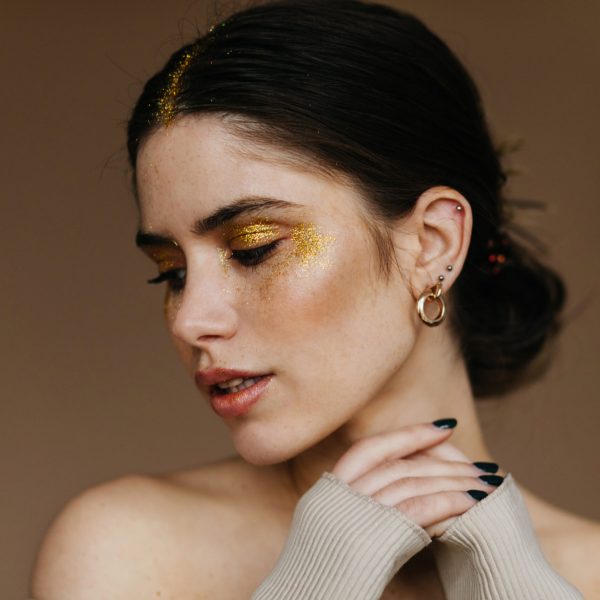 Fashionable girl with trendy earrings chilling in studio. Photo of glad brunette lady with party makeup.